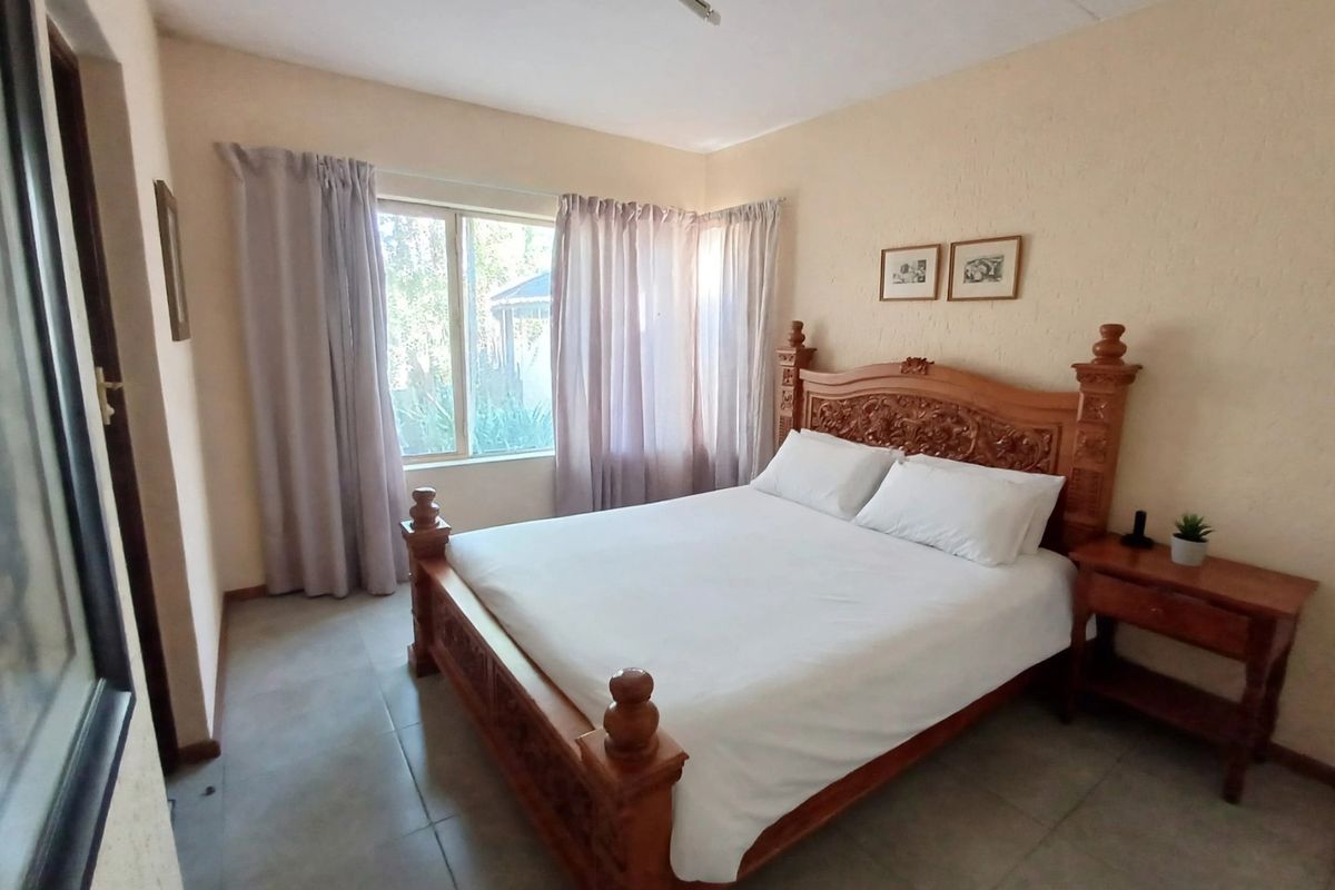A well-lit bedroom featuring neutral wall finishes, tiled flooring, and a large window providing natural light.