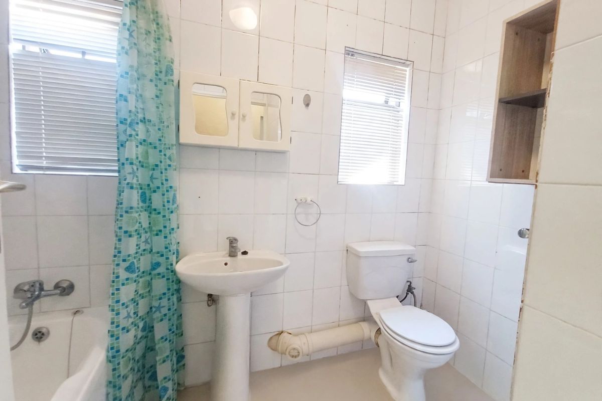 A functional bathroom featuring a pedestal basin, toilet, and bathtub with tiled walls and built-in storage, requiring cosmetic updates.