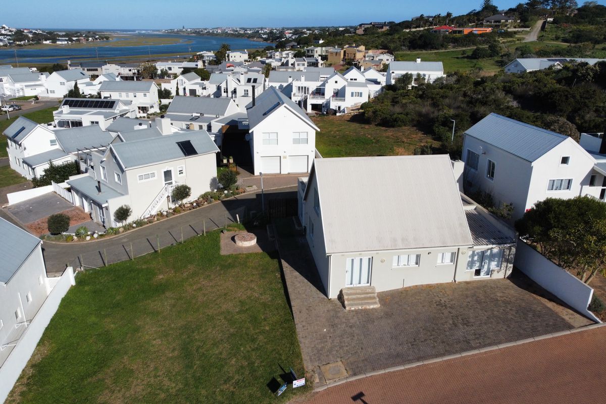 Aerial view of a residential property featuring a paved driveway, lawn, and metal roof, situated within a coastal estate neighborhood.