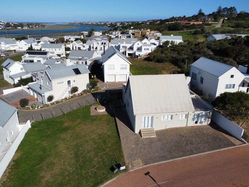 Aerial view of a residential property featuring a paved driveway, lawn, and metal roof, situated within a coastal estate neighborhood.