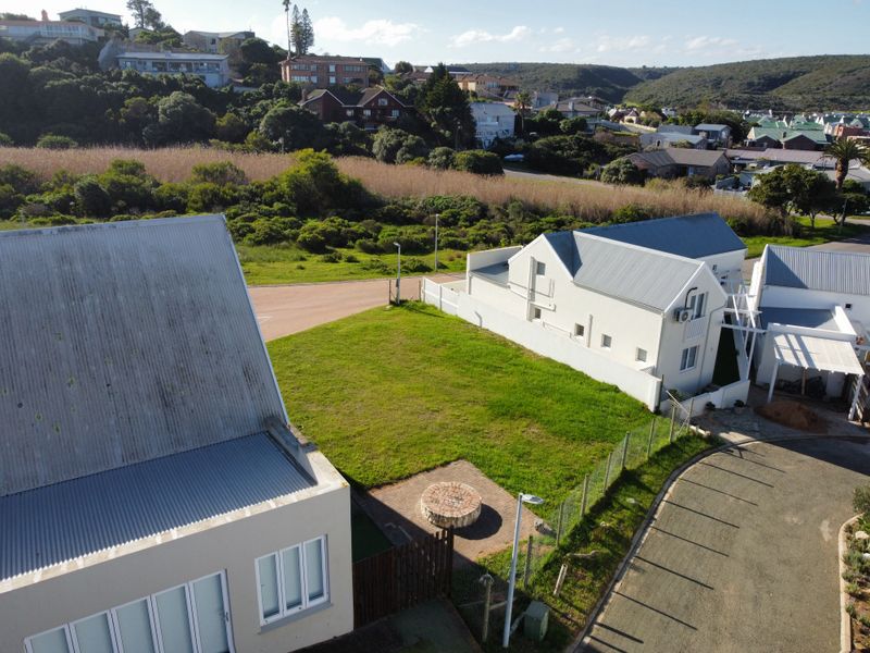 Aerial view of a residential plot featuring a grassed area, brick fire pit, and surrounding neighborhood infrastructure.
