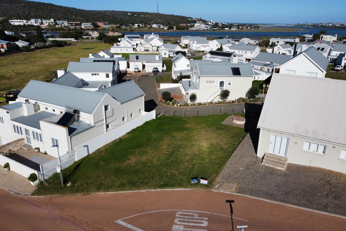 An aerial view of a vacant residential plot situated within a developed coastal estate, featuring paved street access and surrounding established homes.