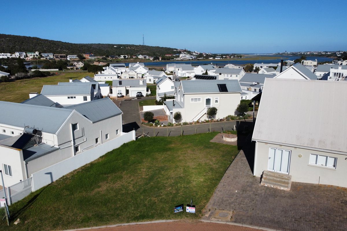Aerial view of a vacant residential plot situated within a developed coastal estate, featuring established surrounding homes and proximity to the lagoon.
