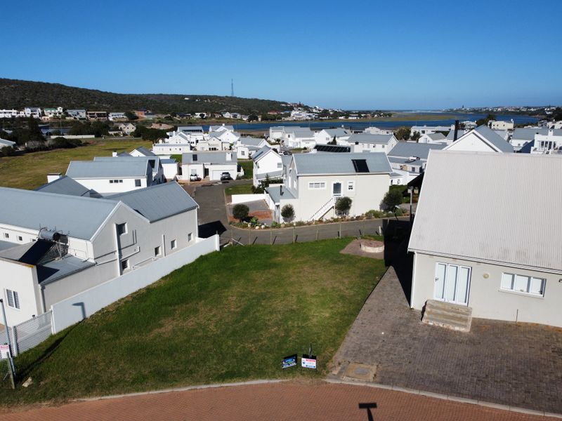 Aerial view of a vacant residential plot situated within a developed coastal estate, featuring established surrounding homes and proximity to the lagoon.