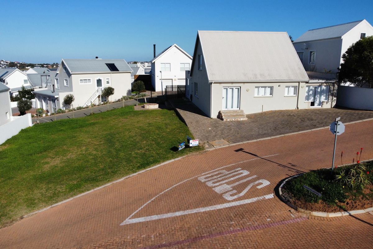 Aerial view of a residential property featuring a paved driveway, well-maintained lawn, and modern house with a metal roof in a quiet neighborhood.