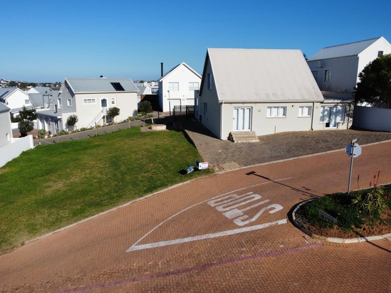 Aerial view of a residential property featuring a paved driveway, well-maintained lawn, and modern house with a metal roof in a quiet neighborhood.