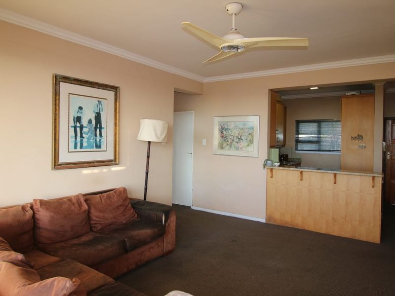Open plan living area featuring a breakfast bar, ceiling fan, and crown molding, connecting to a kitchen space with built-in cabinetry.