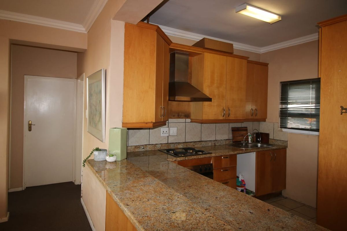 A functional kitchen featuring wooden cabinetry, granite countertops, a built-in hob, and an extractor fan, with a breakfast bar overlooking the adjacent living area.