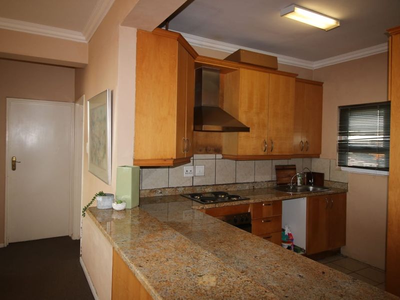 A functional kitchen featuring wooden cabinetry, granite countertops, a built-in hob, and an extractor fan, with a breakfast bar overlooking the adjacent living area.