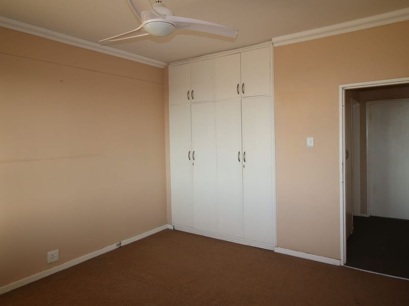 An empty bedroom featuring built-in cupboards, a ceiling fan, and neutral wall finishes, offering a blank canvas for personalization.