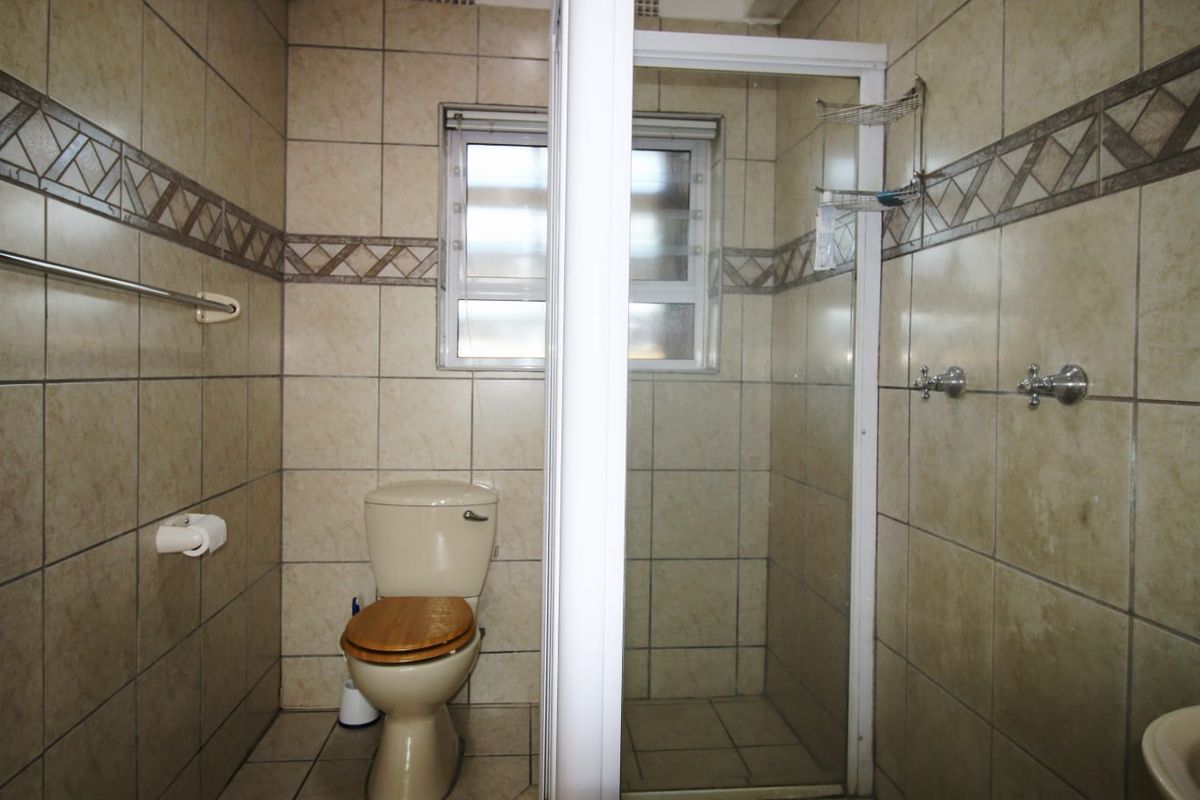 A functional bathroom featuring a shower enclosure, toilet, and fully tiled walls. The space is dated and would benefit from modern updates.