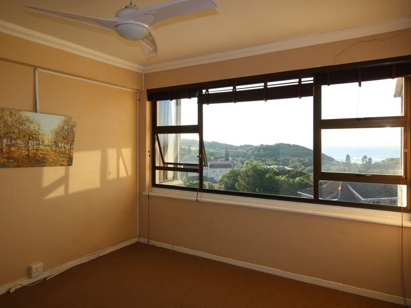 An empty bedroom featuring a ceiling fan, carpeted flooring, and large windows offering scenic coastal and landscape views.