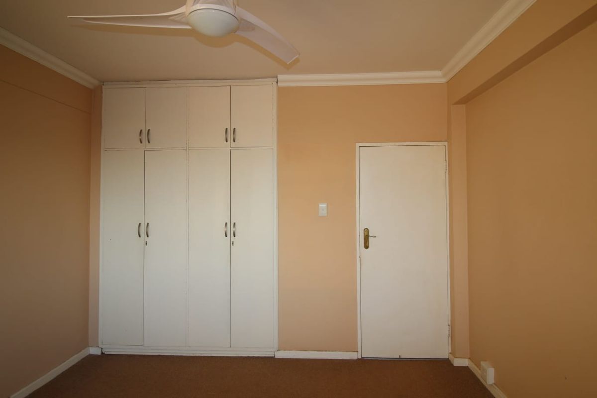 A vacant bedroom featuring built-in cupboards, a ceiling fan, and neutral wall finishes, providing a blank canvas for personalization.
