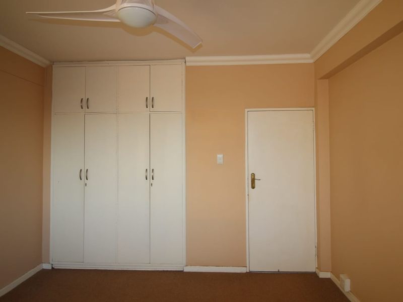 A vacant bedroom featuring built-in cupboards, a ceiling fan, and neutral wall finishes, providing a blank canvas for personalization.