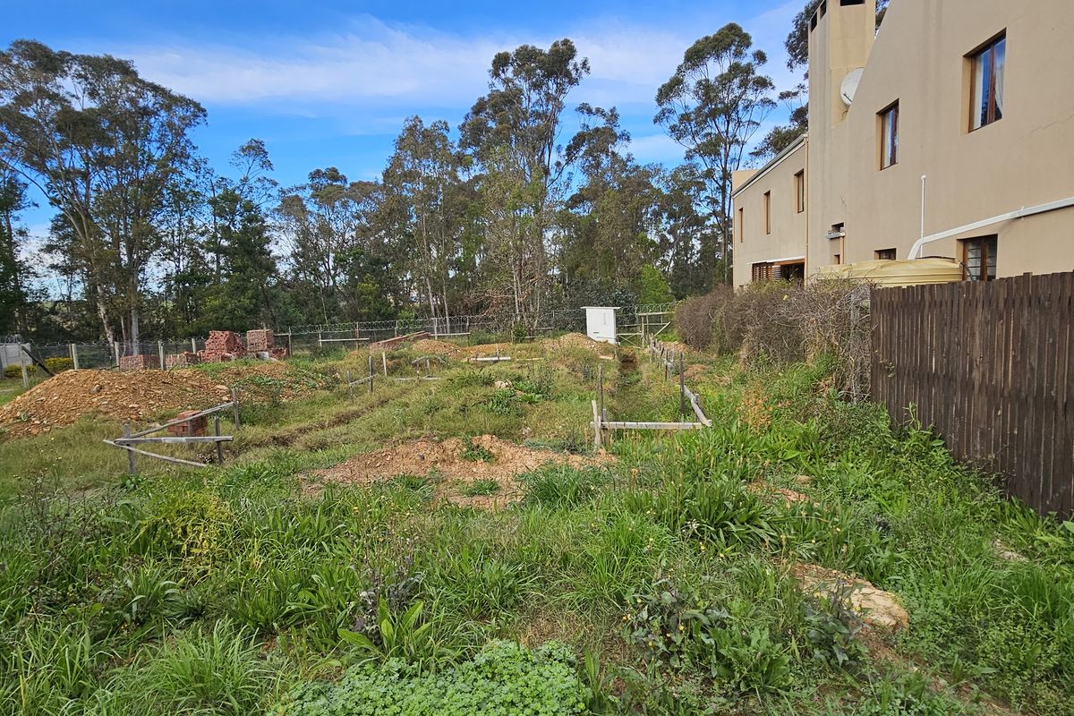 Rear view of a residential property showing an overgrown plot with active foundation trenches and perimeter fencing.