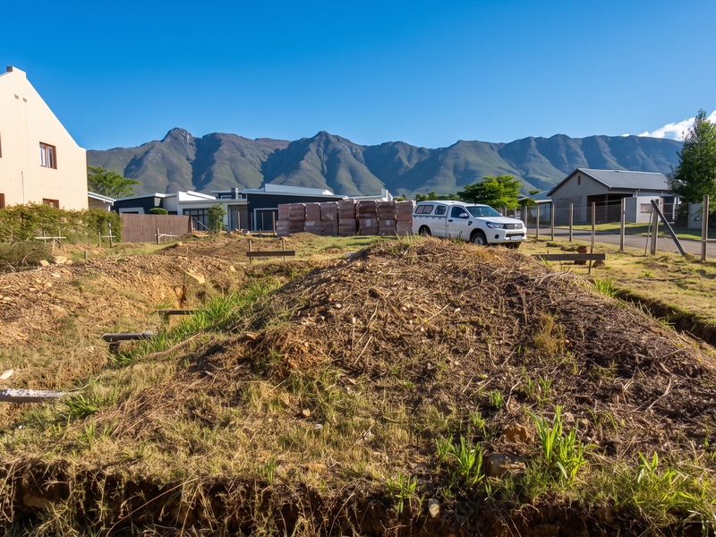 A vacant residential plot showing initial site excavation and preparation work with mountain views in the background.