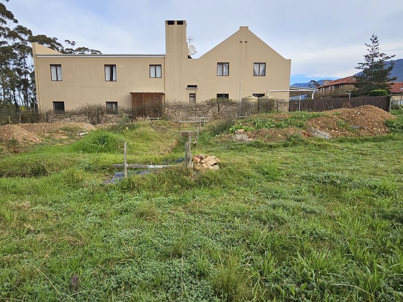 A view of the rear of the property showing an undeveloped, overgrown residential plot with soil mounds and existing boundary walls.