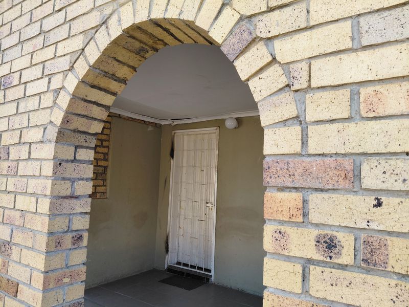 Entrance area featuring a brick archway, tiled porch, and a white security gate.