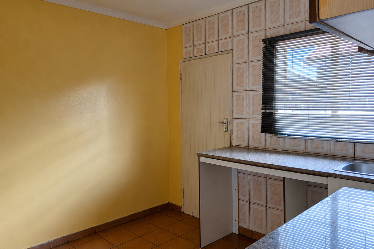 A compact kitchen area featuring tiled splashbacks, laminate countertops, a stainless steel sink, and tiled flooring, currently presented as an empty space.