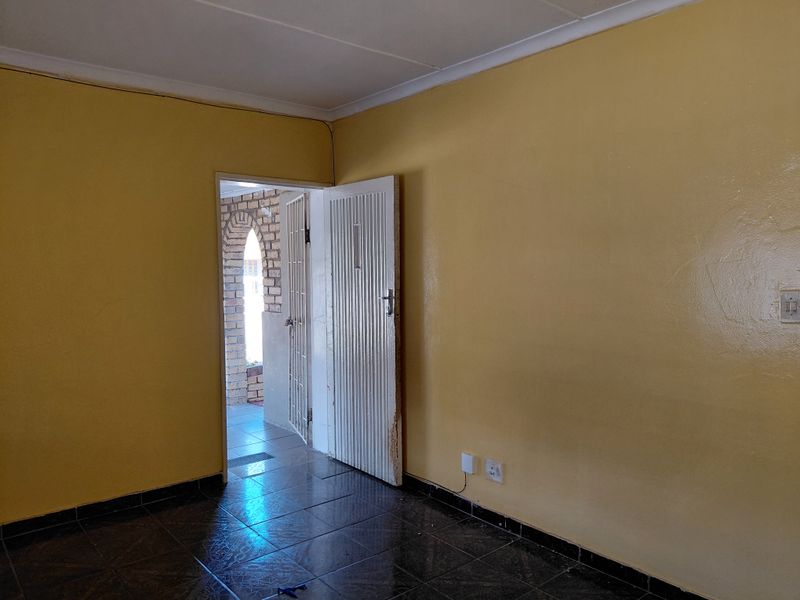 An empty living area featuring tiled flooring, yellow painted walls, and a security gate leading to an exterior space.