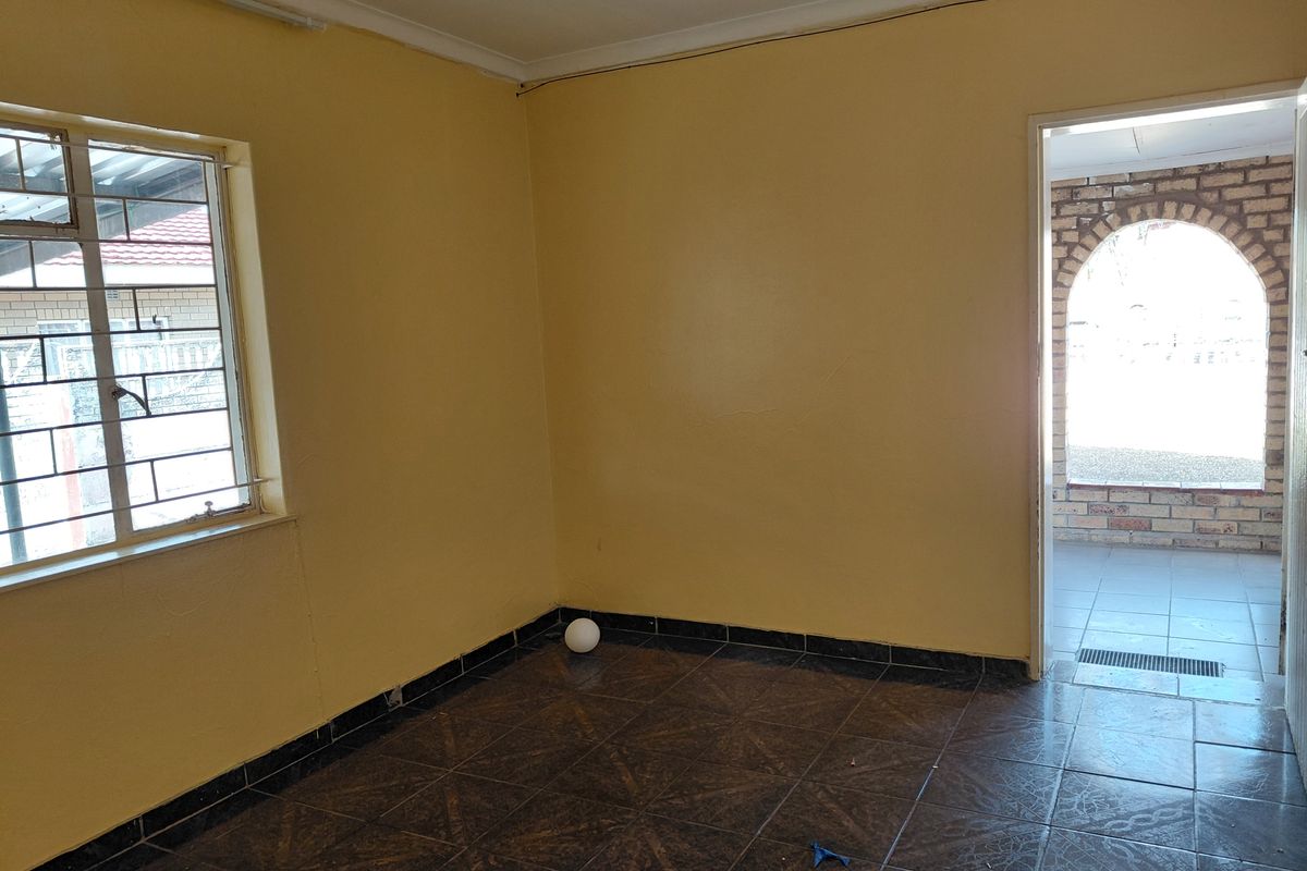 An empty bedroom featuring tiled flooring, security bars on the window, and access to an adjacent outdoor patio area.