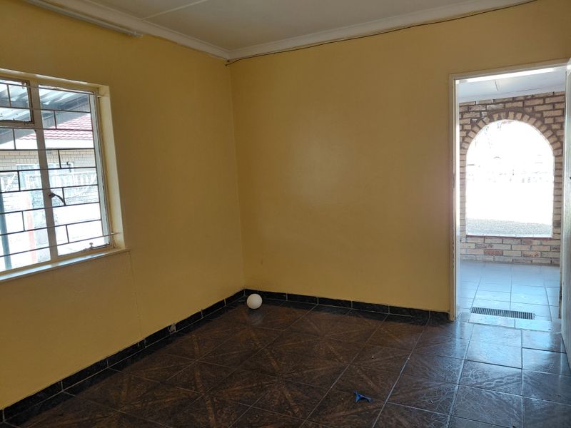 An empty bedroom featuring tiled flooring, security bars on the window, and access to an adjacent outdoor patio area.