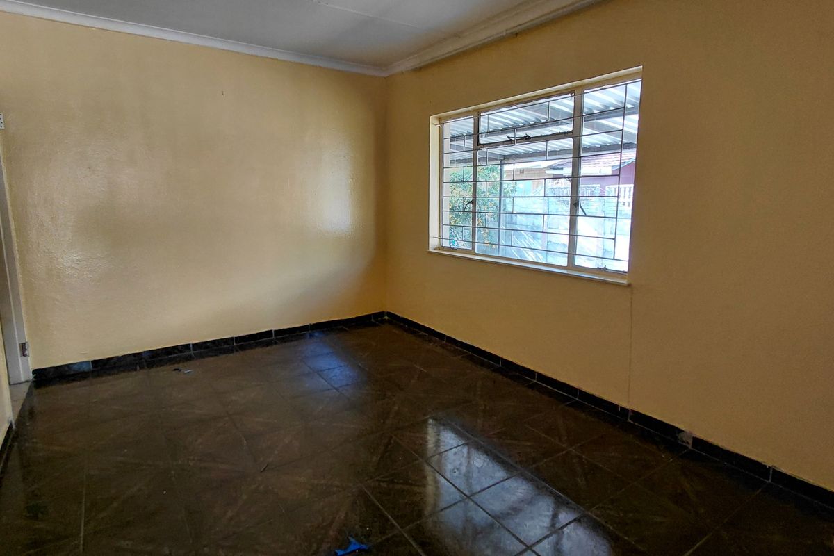 An empty living room featuring dark tiled flooring, yellow painted walls, and a window fitted with security bars.