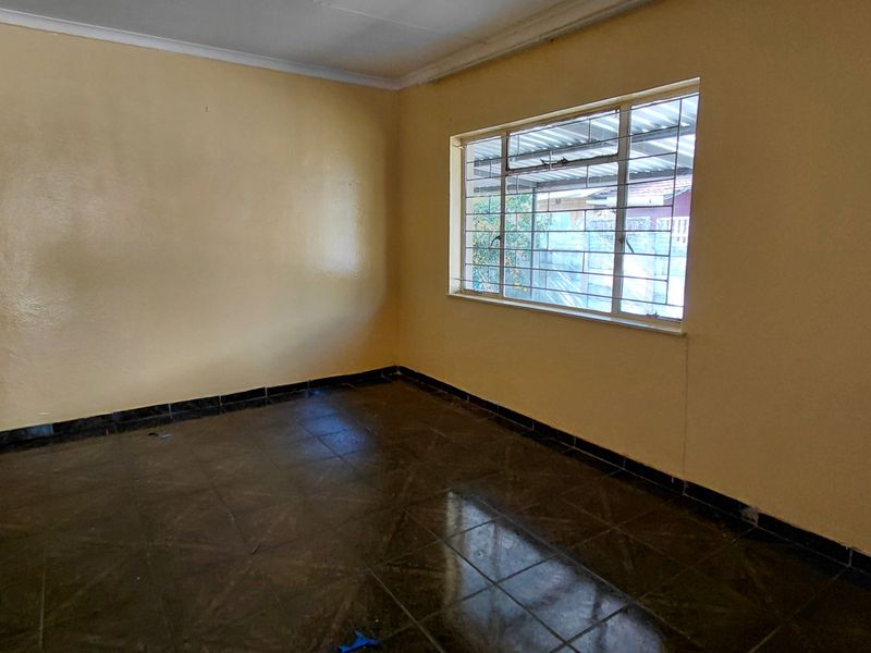 An empty living room featuring dark tiled flooring, yellow painted walls, and a window fitted with security bars.