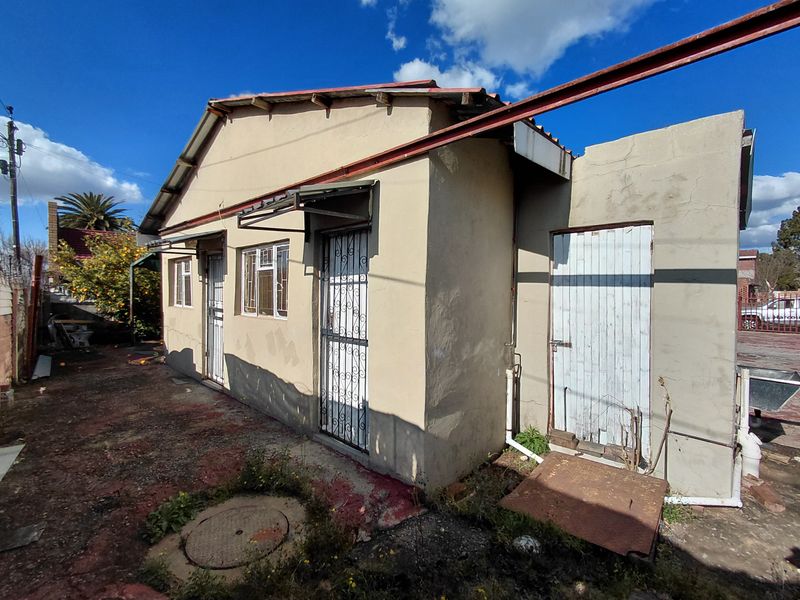 Rear exterior view of the property showing weathered plaster walls, security gates, and a corrugated metal roof in need of maintenance.