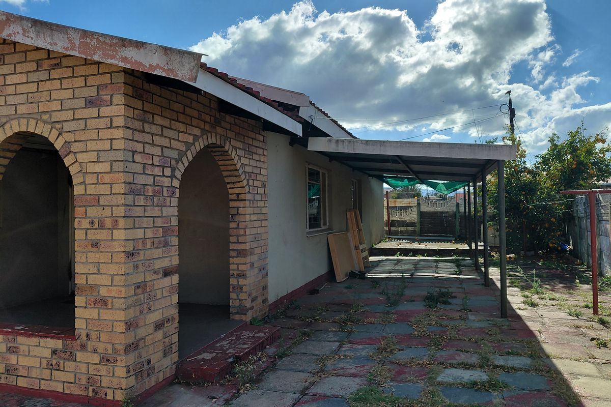 Rear exterior view of the property featuring a brick facade with arched entryway, a covered patio area, and a paved courtyard with garden space.