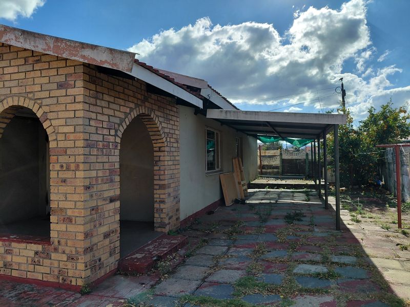 Rear exterior view of the property featuring a brick facade with arched entryway, a covered patio area, and a paved courtyard with garden space.
