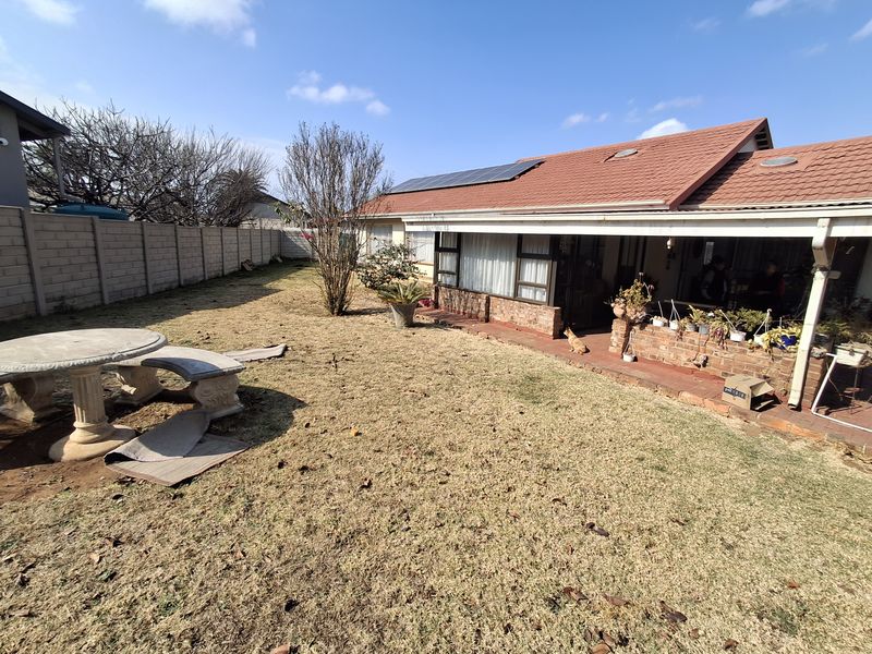 Rear view of the property featuring a covered patio, solar panels on a tiled roof, and a spacious garden with a concrete seating area.