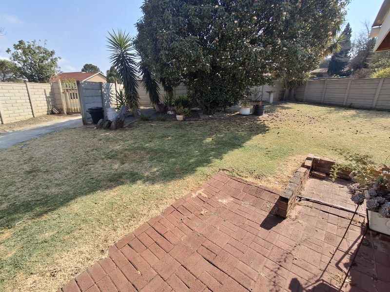 A private backyard featuring a brick-paved patio area, established trees, and a secure precast concrete boundary wall.
