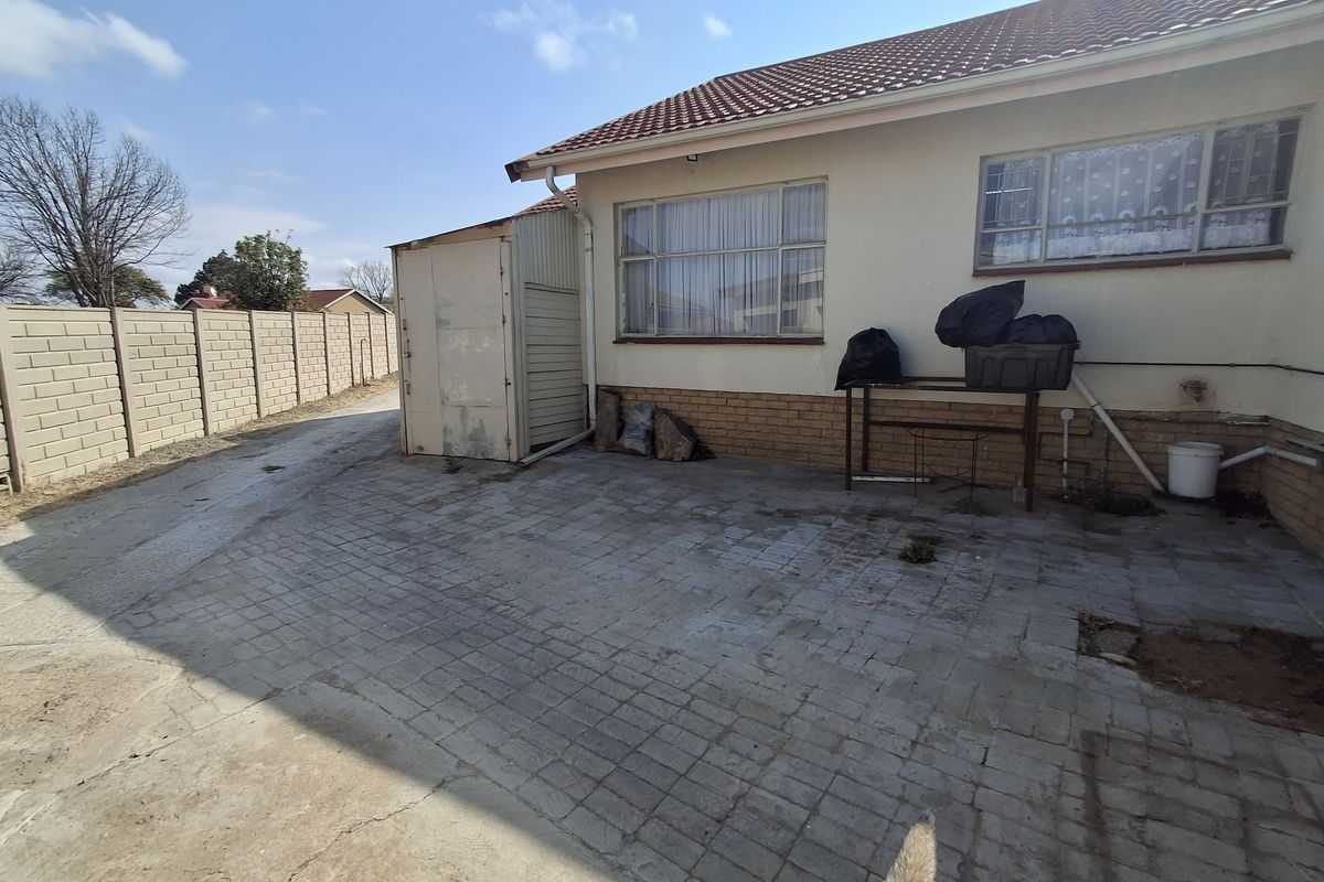 Rear exterior view of the property featuring a paved courtyard, precast boundary wall, and a metal storage shed attached to the main structure.