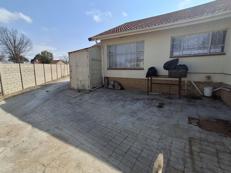 Rear exterior view of the property featuring a paved courtyard, precast boundary wall, and a metal storage shed attached to the main structure.
