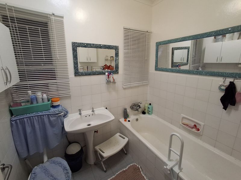 A functional bathroom featuring a pedestal washbasin, a built-in bathtub with wall-mounted fixtures, and tiled wall finishes.