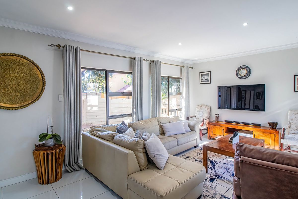 A bright and spacious living room featuring tiled flooring, recessed downlighting, and large aluminium-framed windows that provide ample natural light.
