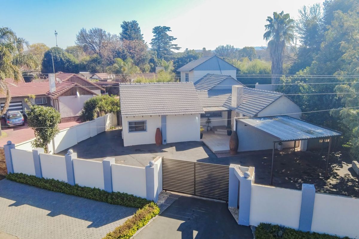 Aerial view of the property featuring a tiled roof house, paved driveway, secure perimeter wall with sliding gate, and a covered carport area.