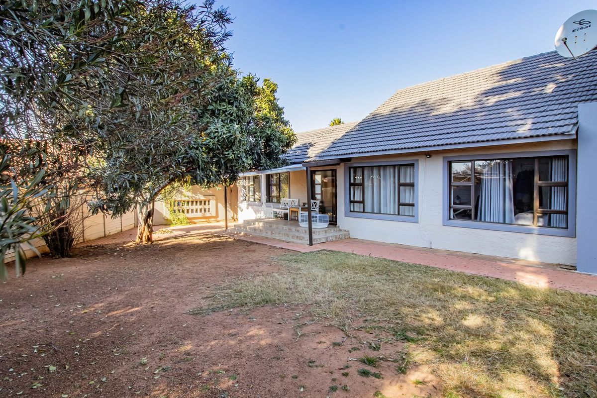 Rear view of the house featuring a tiled roof, paved walkway, and established garden area with mature trees.