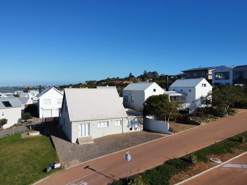 Aerial view of a residential property featuring white exterior walls, metal roofing, and a paved driveway in a coastal neighborhood setting.