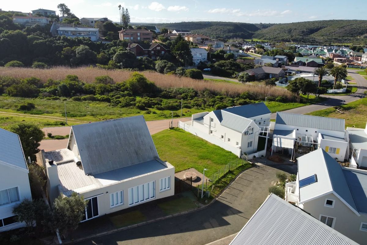Aerial view of a residential property featuring multiple detached homes with metal roofing, paved driveways, and surrounding landscaped grounds in a coastal estate setting.