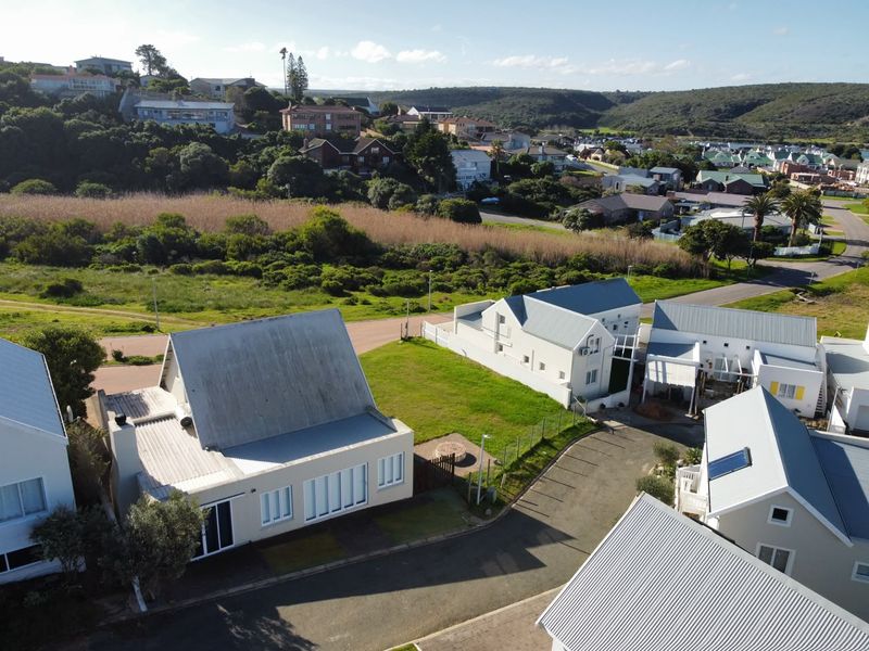 Aerial view of a residential property featuring multiple detached homes with metal roofing, paved driveways, and surrounding landscaped grounds in a coastal estate setting.