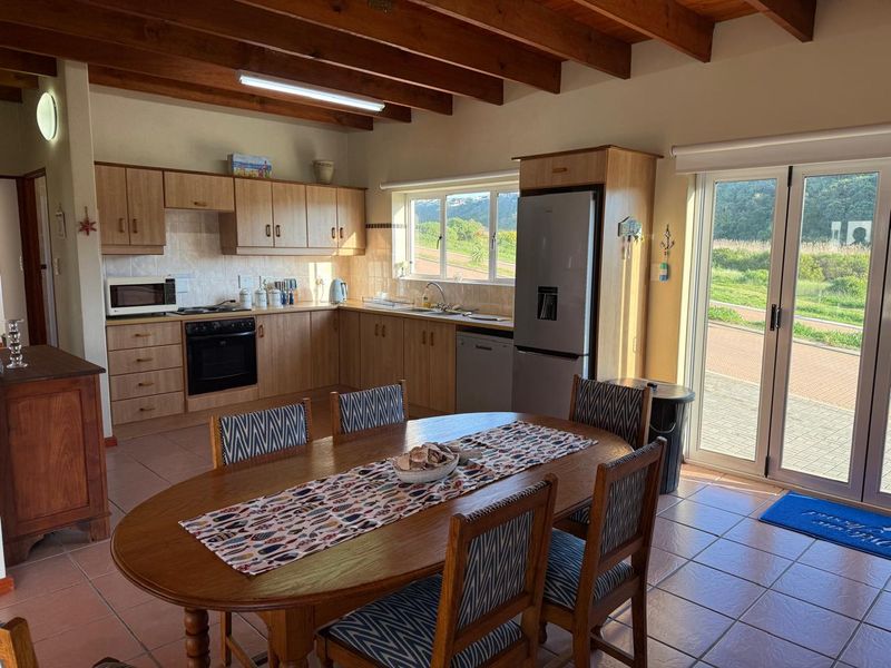 Open-plan kitchen and dining area featuring exposed timber beams, tiled flooring, and direct access to the outdoors through double glass doors.