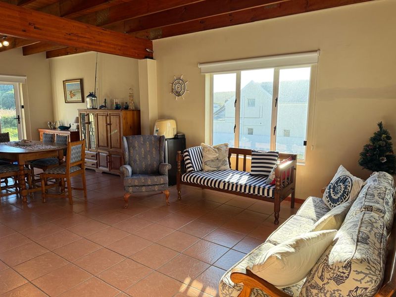 Spacious open-plan living and dining area featuring exposed timber ceiling beams, ceramic tiled flooring, and large windows providing ample natural light.
