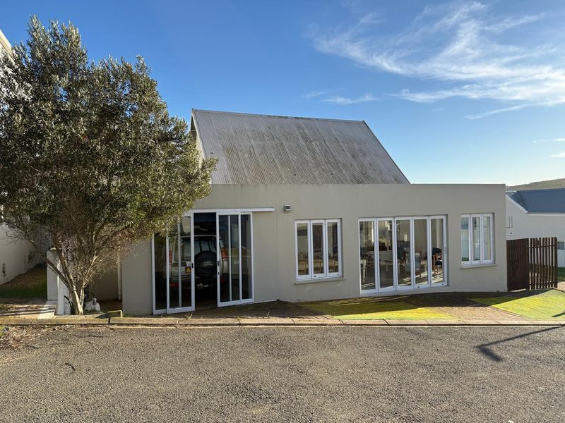 Front exterior view of a house featuring a corrugated metal roof, white-framed sliding glass doors, and casement windows with a paved driveway area.