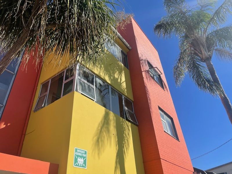 A low-angle view of a multi-story apartment building facade featuring vibrant yellow and orange painted brickwork and aluminium-framed casement windows.