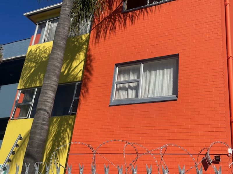 Exterior view of a multi-story flat building featuring a brightly painted brick facade and security razor wire fencing.