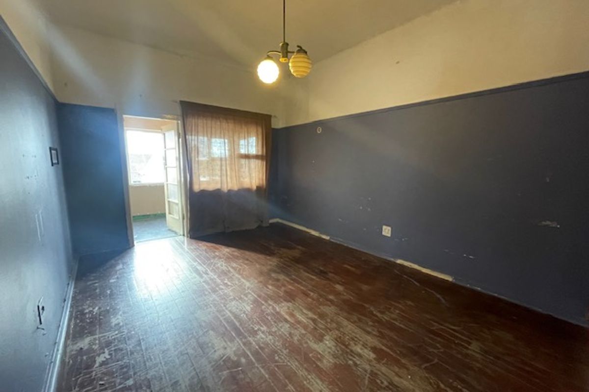 An empty living room featuring original hardwood flooring, picture rails, and access to an adjoining balcony area.