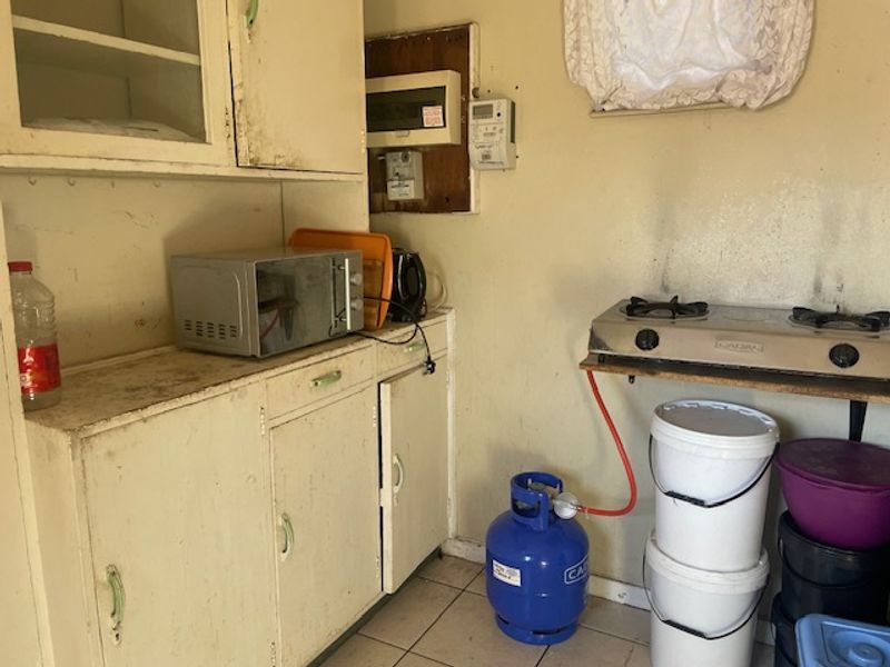 A dated kitchen area featuring basic built-in cabinetry, a gas hob, and an exposed electrical distribution board, requiring significant cosmetic updates.