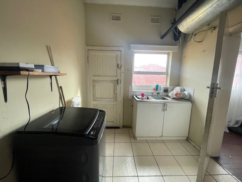 A functional laundry area featuring tiled flooring, a sink with cabinetry, and wall-mounted shelving, requiring cosmetic updates to improve its overall condition.